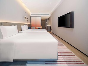 Une chambre d’hôtel moderne avec un grand lit, un téléviseur fixé au mur et une petite table avec une chaise.