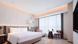 A modern hotel room with a large bed, a small round table, a sofa, and a TV. - Novotel Xiamen Downtown (Xiamen)