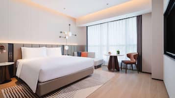 A modern hotel room with a large bed, a small round table, a sofa, and a TV.