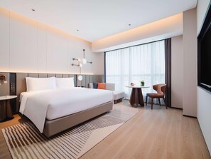 A modern hotel room with a large bed, a small round table, a sofa, and a TV. - Novotel Xiamen Downtown (Xiamen)