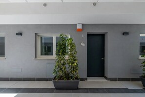 A modern building with a grey facade, a large planter with greenery, and a door marked with the number 5.