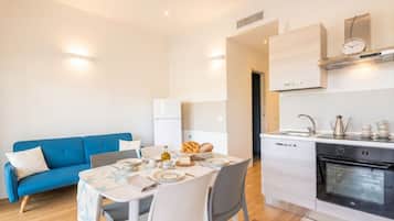 Una cucina moderna con forno integrato, un'area pranzo con tavolo apparecchiato per due e un divano blu nella zona soggiorno.