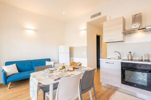 A modern kitchen with a built-in oven, a dining area with a table set for two, and a blue sofa in the living area. - Domus Blaesia - Cozy Stay (Bari)