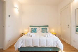 A double bed with a teal headboard, white bedding, and two bedside tables with lamps.