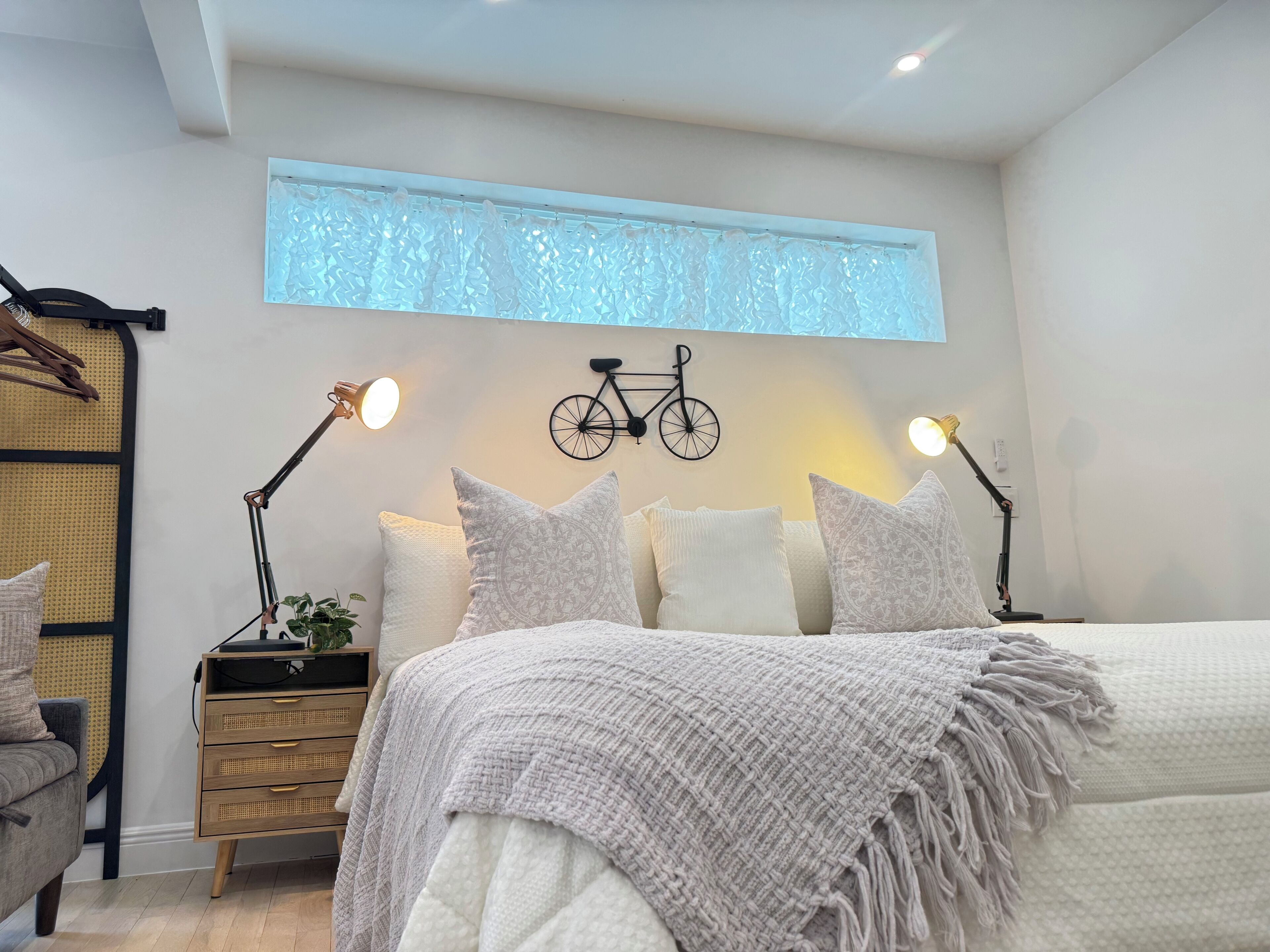 A bedroom with a bed, bedside tables, a bicycle wall decoration, and a window with a textured blind.