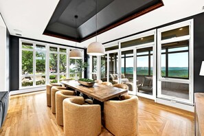 Un vaste espace dédié à la salle à manger, avec une table et des chaises en bois, de grandes fenêtres et une vue sur l’extérieur.