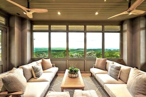 A room with two sofas facing a large window, a wooden coffee table, and a ceiling fan.