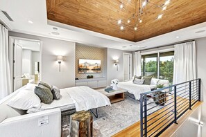 Quarto moderno com duas camas, uma janela grande e teto de madeira.