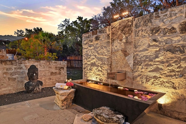 En stenvæg med et vandfald, en Buddha-statue og et lille bord med blomster.