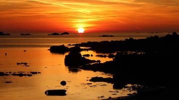 Ein Sonnenuntergang über einem ruhigen Meer mit Felsformationen und in der Ferne Inseln.