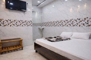 A modern bedroom with a marble-patterned wall, a wooden bench, a bed with a floral bedspread, and a mounted TV. - Hotel Relax Kurla  (Mumbai)