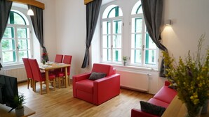 Een moderne woonkamer met een eethoek, met rode meubels, grote ramen en een radiator.