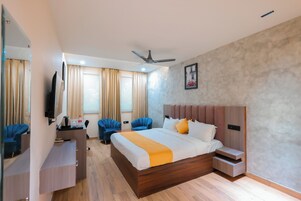 Una habitación de hotel moderna con una cama grande, un escritorio, dos sillas, un televisor y un ventilador de techo.