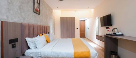 A modern hotel room with a large bed, bedside table, and a desk with a TV.