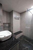 Un baño moderno con un lavamanos blanco, encimera de mármol negro y cabina de ducha de vidrio.