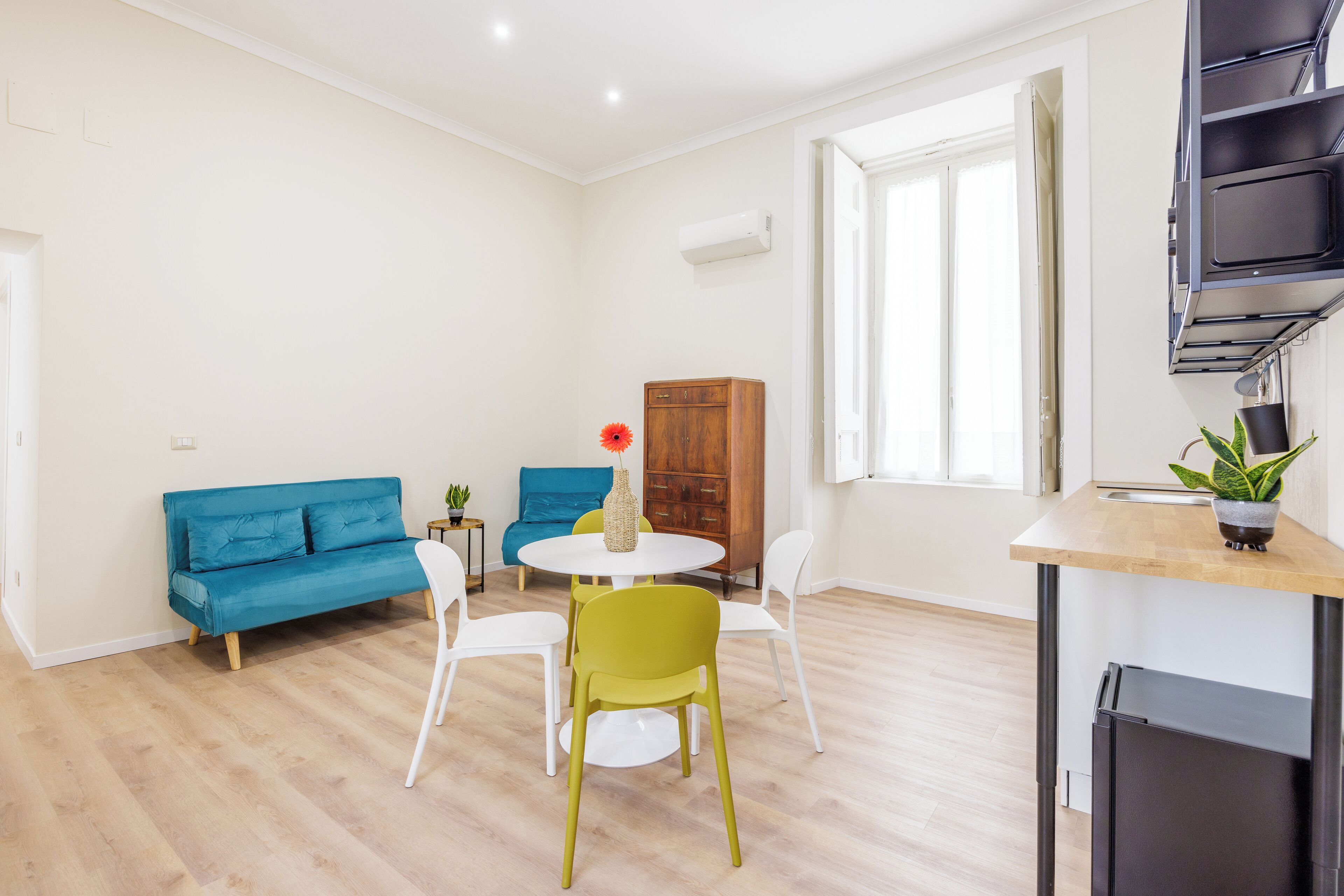 Una sala moderna con un sofá azul, un sillón verde, una mesa blanca y un armario pequeño.