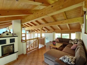 Un'ampia zona giorno con soffitto in legno, camino, divano e tavolo da pranzo.
