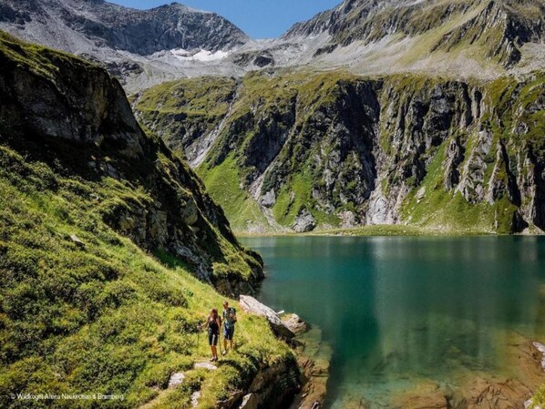 Paisaje montañoso con un lago cristalino y excursionistas en un sendero.