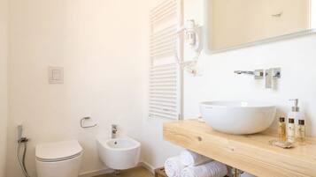 A bathroom with a toilet, bidet, and a large white sink on a wooden countertop.
