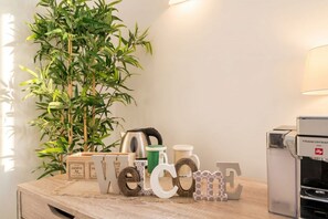 Un tavolo di legno con un cartello con la scritta 'Welcome', una tazza verde, una tazza bianca, una tazza nera, un bollitore d'argento e una macchina per il caffè.