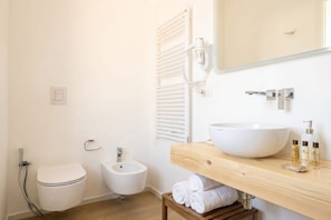 Ein Badezimmer mit Toilette, Bidet und einem groĂen weiĂen Waschbecken auf einer Holzauslage.
