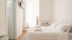 A minimalist bedroom with a bed, a chair, and a small table with bottles.