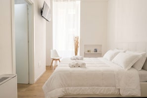 Ein schlicht eingerichtetes Schlafzimmer mit einem Bett, einem Sessel und einem kleinen Tisch mit Flaschen.
