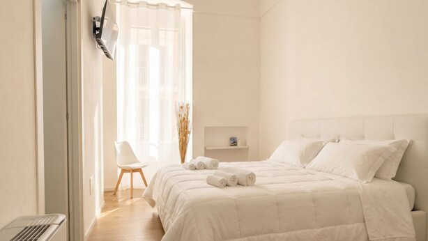 A bedroom with a bed, a chair, a shelf, and a radiator.
