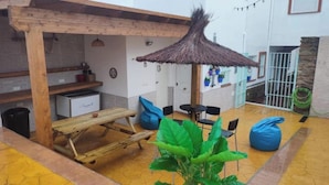 Un patio con mesa y sillas de madera, un paraguas de paja y plantas en macetas.