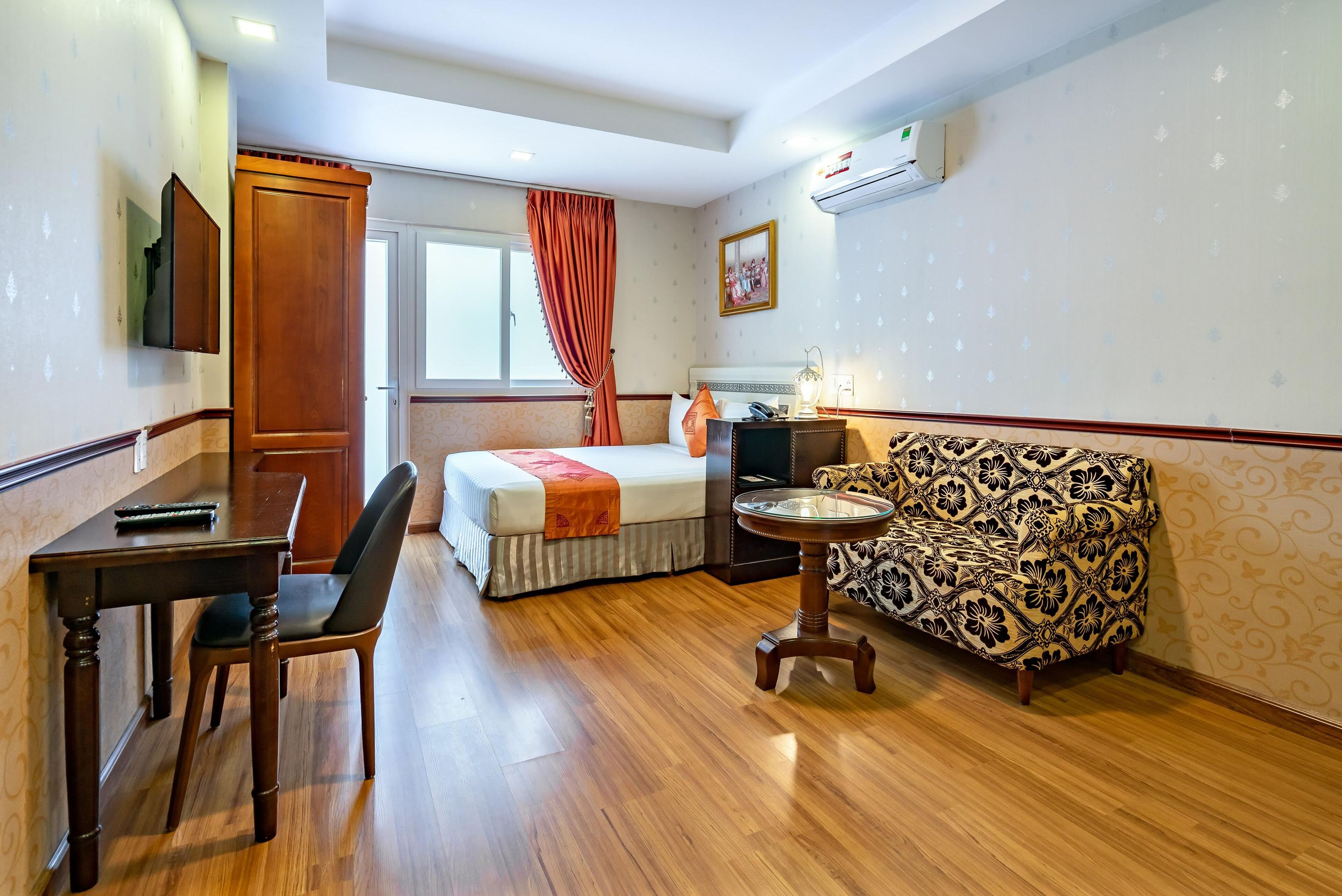 Ein Hotelzimmer mit einem Bett, einem Schreibtisch, einem Sessel, einer gemusterten Couch, einem kleinen Tisch und einem Fenster mit Vorhängen.