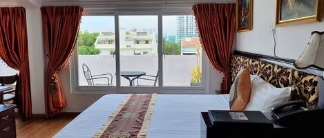 Habitación de hotel con una cama grande, un escritorio, una silla y vistas a edificios desde la ventana.