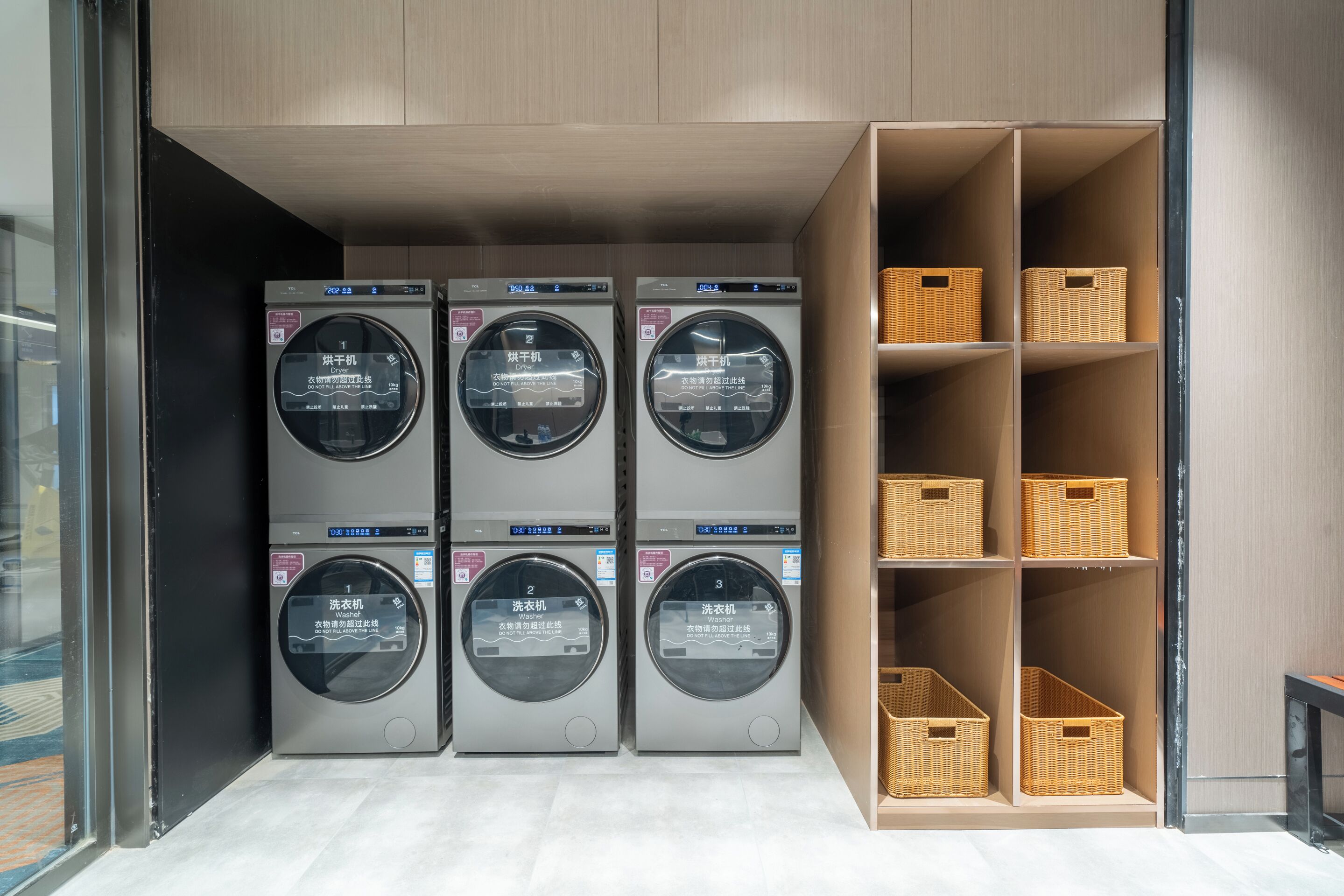 A laundry facility with four washing machines and shelves with baskets.