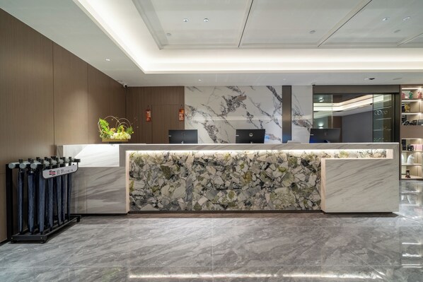 A modern reception desk with a marble counter, a plant, and a digital display.