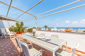 Una terrazza con tavolo e sedie, vista su una spiaggia e il mare.