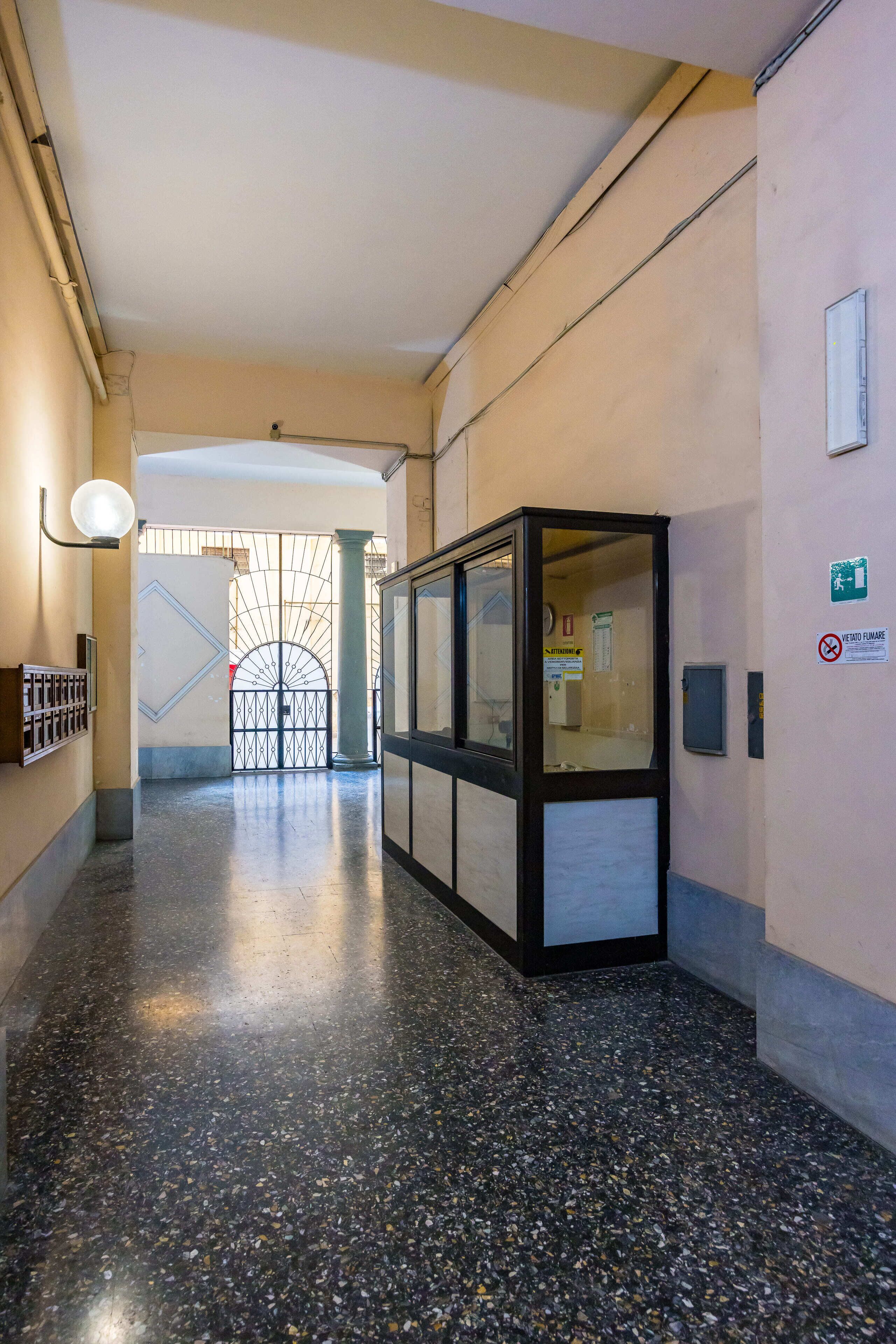 A corridor with a glass display case, a light fixture, and a door with a sign.