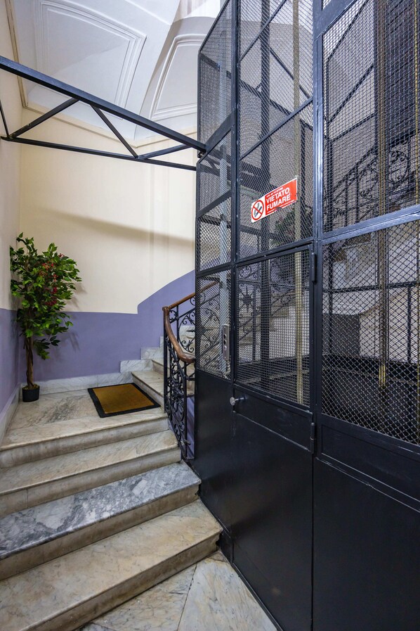 Un escalier avec des marches en marbre, une plante en pot et un portail en métal noir avec une plaque.
