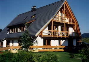 Ein zweistöckiges Haus mit Balkon, Schornstein und einem Auto auf der Auffahrt.