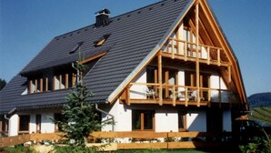 A house with a steeply pitched roof, wooden balcony, and a fenced yard. - 4-Star Superior Apartment (80 sqm) with Mountain View, Shared Terrace & Wi-Fi (Hinterzarten)
