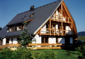 Une maison avec un toit à forte pente, un balcon en bois et une cour clôturée.