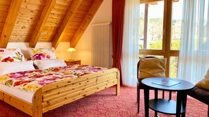 A bedroom with a wooden bed, a nightstand, a lamp, a chair, and a window with curtains. - 4-Star Superior Apartment (80 sqm) with Mountain View, Shared Terrace & Wi-Fi (Hinterzarten)