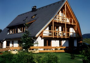 A two-story house with a sloped roof, wooden balcony, and a small tree in the foreground. - Apartment 'Studio – With Balcony 40 sqm' with Mountain View, Shared Terrace and Wi-Fi (Hinterzarten)