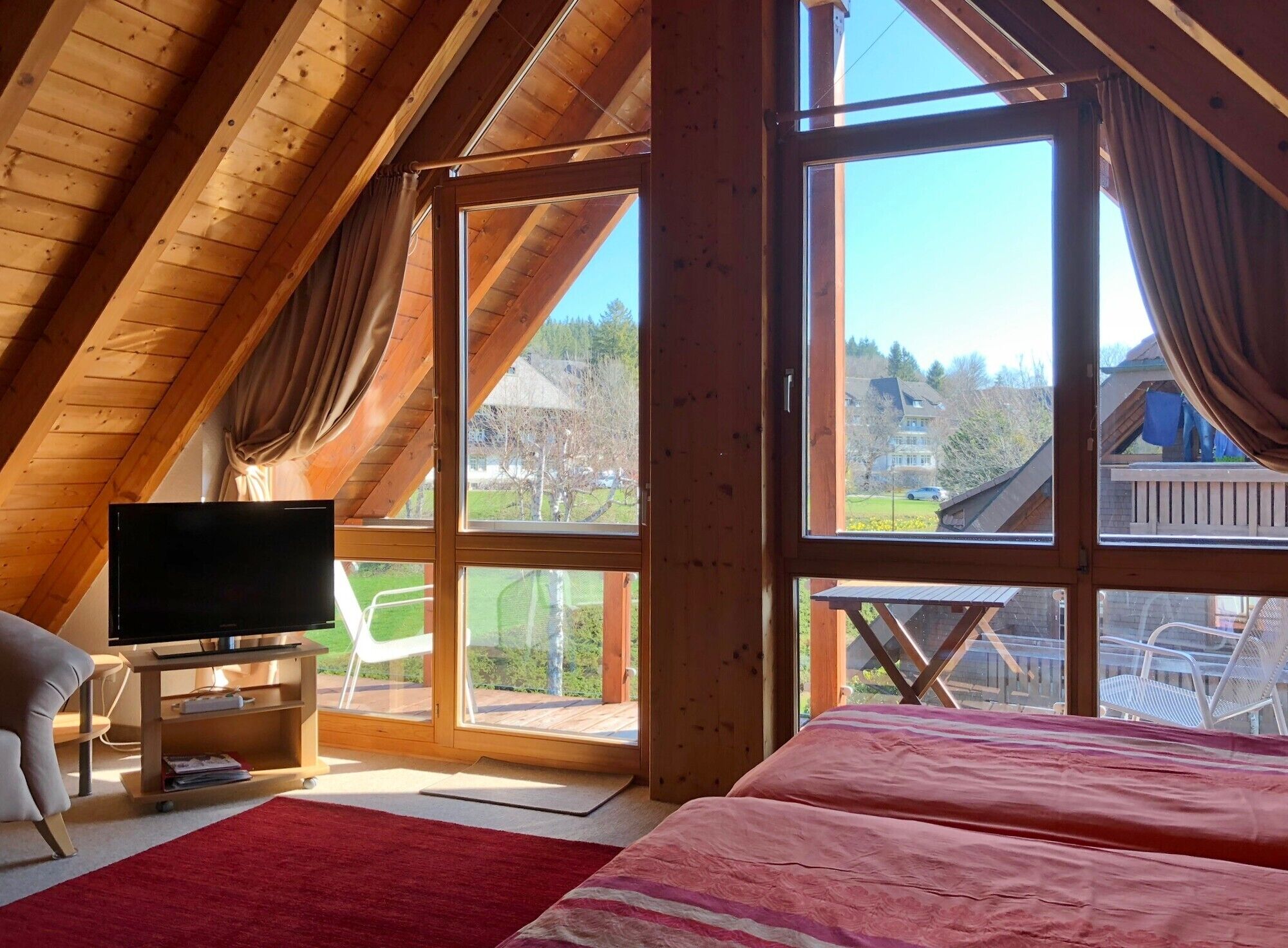 Een slaapkamer met een televisie, een bed, een stoel en grote ramen.