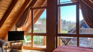 A bedroom with a TV, a bed, a chair, and large windows. - Apartment 'Studio – With Balcony 40 sqm' with Mountain View, Shared Terrace and Wi-Fi (Hinterzarten)