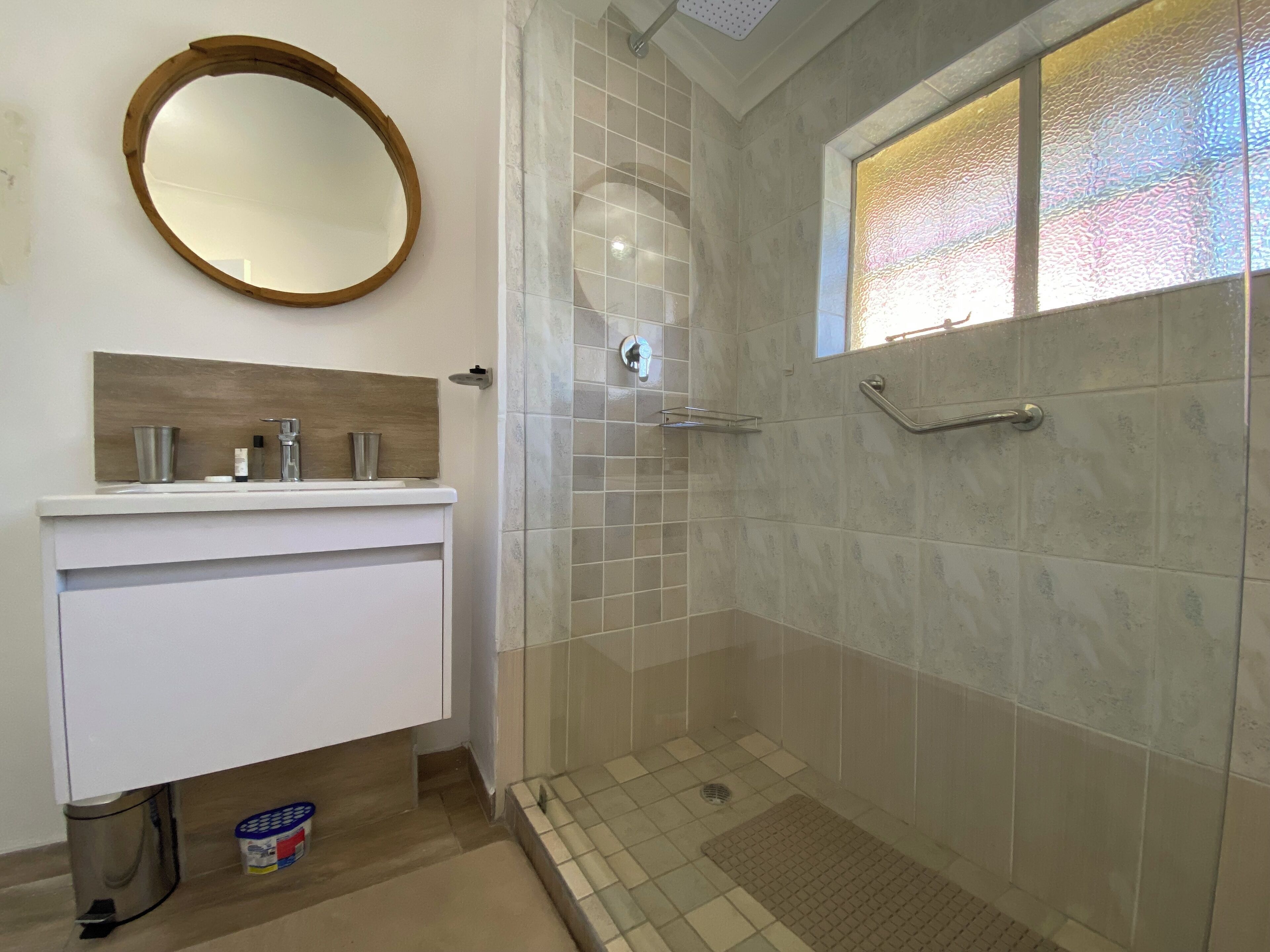 A bathroom with a shower, a sink with a mirror, and a window with frosted glass.