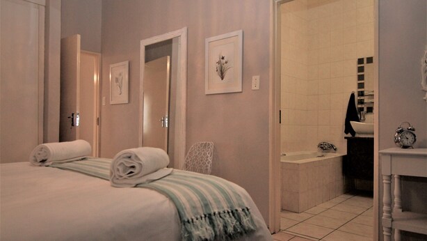 Une chambre d’hôtel avec un lit, une salle de bain avec une baignoire et un réveil sur une table de chevet.