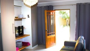 Un salon avec un canapé, un téléviseur posé sur une étagère, un lustre et une porte donnant sur l’extérieur.
