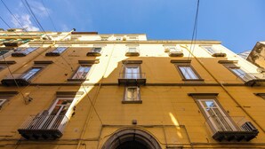 Un edificio amarillo de varios pisos con varios balcones, una entrada arqueada central y numerosas ventanas.