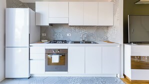 Una cucina moderna con mobili bianchi, forno integrato, lavello in acciaio inossidabile e schienale piastrellato.