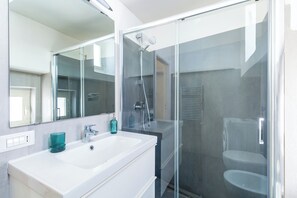 A modern bathroom with a glass-enclosed shower, a white sink, and a mirror above it. - Chiaia Relax on Pedastrian Area (Naples)