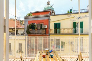 A balcony with a view of a building with a green dome, a fence, and a table with cups and a pot. - Chiaia Relax on Pedastrian Area (Naples)
